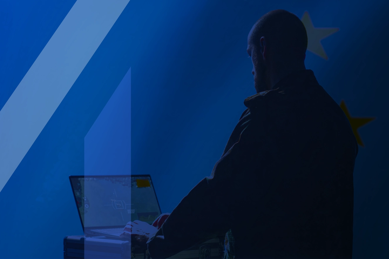 A person on their laptop. Blue tint on the image with the letter M appearing on the side.