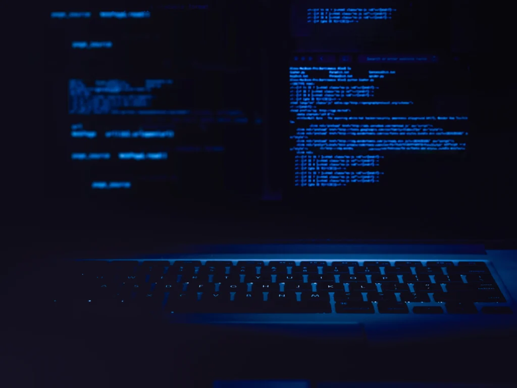 A dark photo of a laptop with blue backlight and some code on the screen