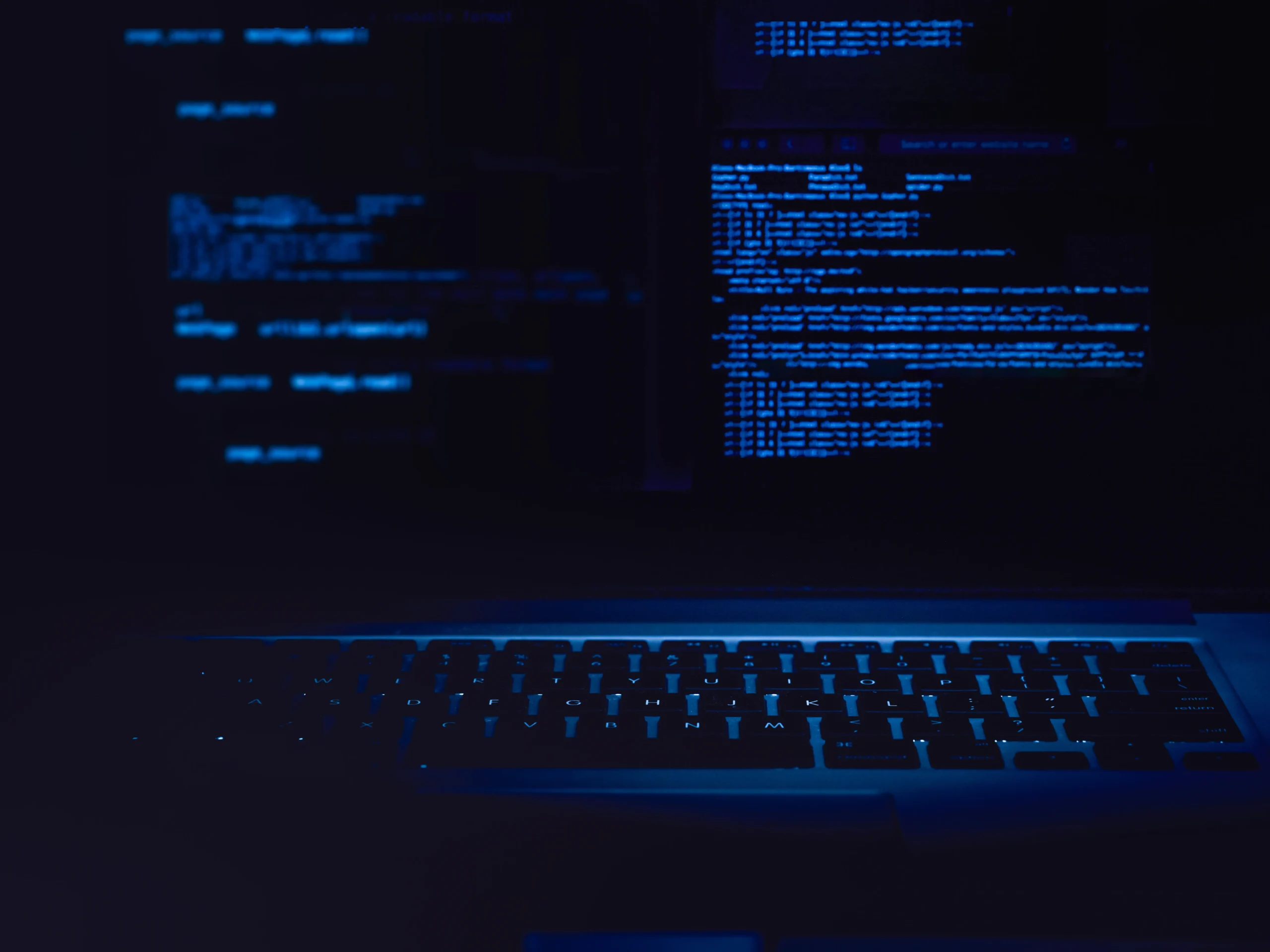 A dark photo of a laptop with blue backlight and some code on the screen